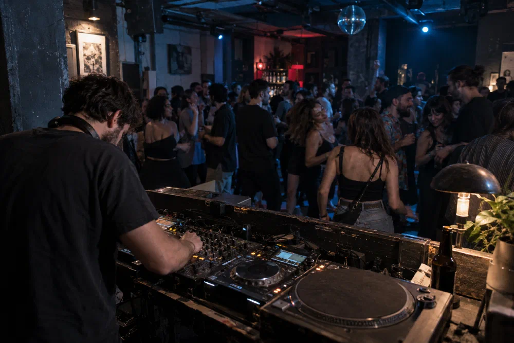 Illustrative scene of a DJ at a mixer with dancers in an intimate blue-lit venue