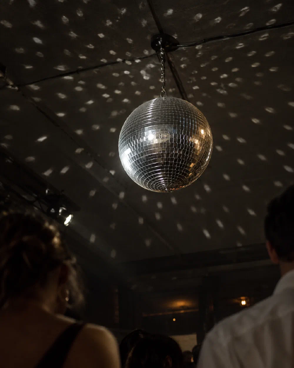 Illustrative scene of a suspended disco ball scattering reflections above party guests