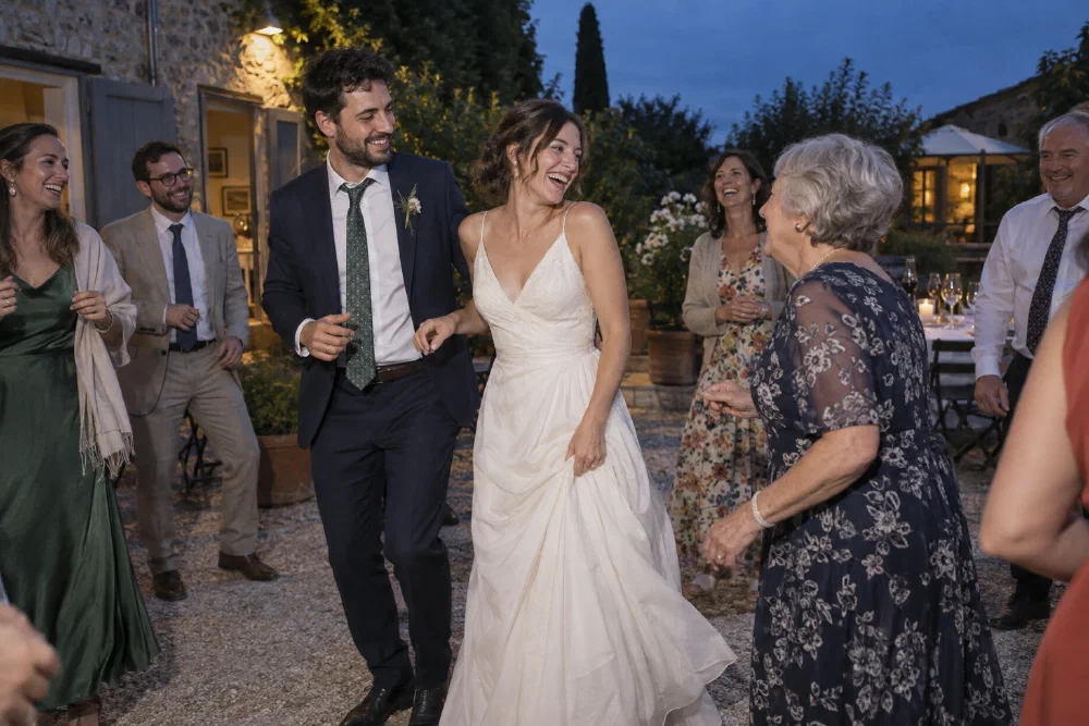 Illustrative scene of a wedding couple dancing with an older guest in a courtyard at blue hour